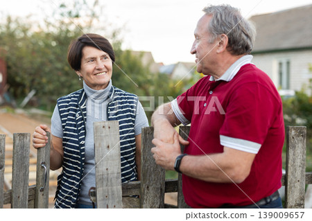 Positive mature man and woman standing near fence in garden Positive mature man and woman standing near fence in garden 139009657