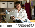 Man seamstress operating by sewing machine, manufactures clothing 139009658
