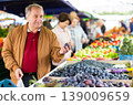 Positive mature male holding plum while choosing fruits and vegetables at market 139009659