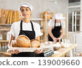 Female baker with basket of aromatic baguettes in bakery 139009660