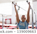 Woman gymnast performs complex acrobatic exercise on parallel bars in gym 139009663