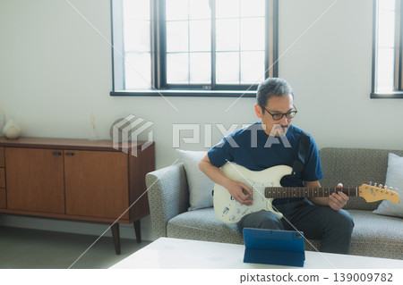 A senior man playing the guitar on a sofa. 139009782