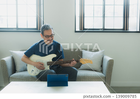 一位老人在沙發上彈吉他。 139009785