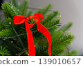 Red ribbon bow on top of Christmas tree with green pine branches 139010657