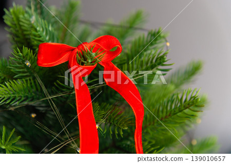 Red ribbon bow on top of Christmas tree with green pine branches Red ribbon bow on top of Christmas tree with green pine branches 139010657
