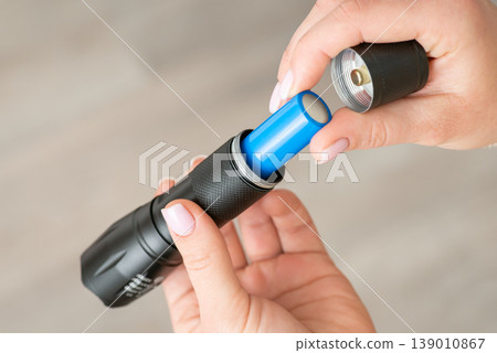 Inserting 18650 battery into flashlight, close up. Small portable pocket device for lighting at darkness in female hands Inserting 18650 battery into flashlight, close up. Small portable pocket device for lighting at darkness in female hands 139010867