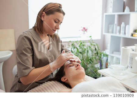 Washing and cleaning the face of girl client before cosmetology procedure. Cosmetologist gets ready for ultrasonic face cleaning procedure in professional beauty salon Washing and cleaning the face of girl client before cosmetology procedure. Cosmetologist gets ready for ultrasonic face cleaning procedure in professional beauty salon 139010909
