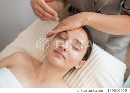 Beautiful young woman enjoying face massage during beauty treatment in the spa, close up. Beauty procedure, relaxation, skin and health care concepts Beautiful young woman enjoying face massage during beauty treatment in the spa, close up. Beauty procedure, relaxation, skin and health care concepts 139010919