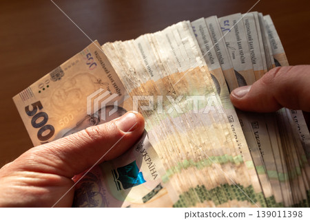 Male hands holding a big stack of ukrainian 500 banknotes, counting them. Good earnings, wealth, savings and payments concepts Male hands holding a big stack of ukrainian 500 banknotes, counting them. Good earnings, wealth, savings and payments concepts 139011398