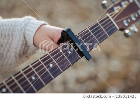 Girl guitarist clinging capo to guitar. Play the guitar using a capo (musical device) Girl guitarist clinging capo to guitar. Play the guitar using a capo (musical device) 139011423