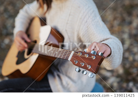 Girl tune acoustic guitar. Close up of hands of a musician tuning guitar outdoor in autumn park Girl tune acoustic guitar. Close up of hands of a musician tuning guitar outdoor in autumn park 139011425