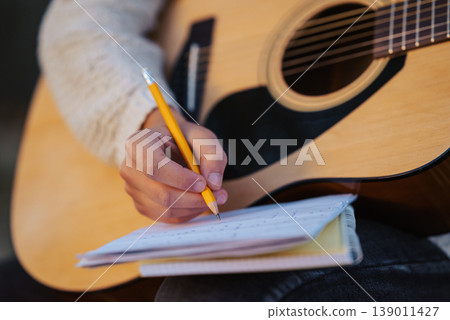 Close up of a girl musician composing song, writing down chords to the notes. Playing the guitar, composing new songs Close up of a girl musician composing song, writing down chords to the notes. Playing the guitar, composing new songs 139011427