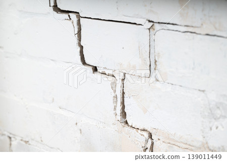 Crack on the white brick wall. Concept of ruining building errors while building structures, deterioration of building 139011449