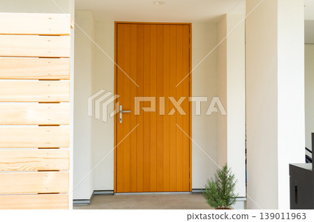 A modern wooden front door that stands out against the white exterior walls. A modern wooden front door that stands out against the white exterior walls. 139011963