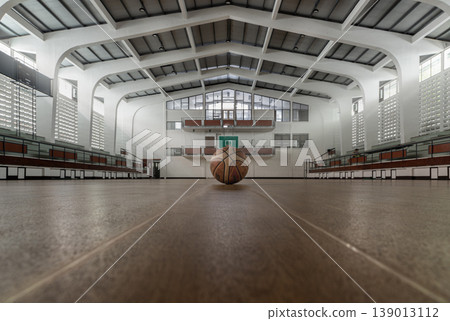 There is a profound stillness in a space designed for noise. Here, white architectural ribs soar toward a vaulted ceiling, framing a lone basketball in a glow of natural light. This low-angle There is a profound stillness in a space designed for noise. Here, white architectural ribs soar toward a vaulted ceiling, framing a lone basketball in a glow of natural light. This low-angle 139013112