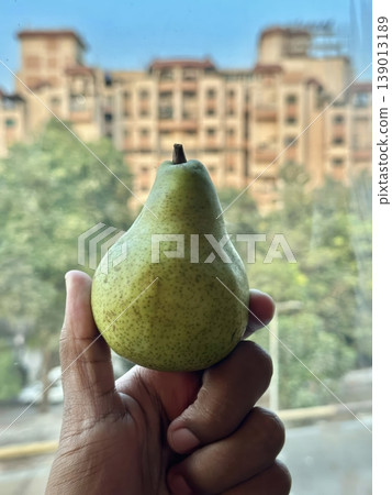 Person Holding a Fresh Green Pear with a Blurred Urban Cityscape Background Person Holding a Fresh Green Pear with a Blurred Urban Cityscape Background 139013189