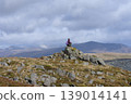 Hiker sitting on mountain peak enjoying vista 139014141