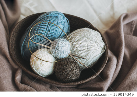 Skeins and balls of woolen yarn and knitting needles for hand knitting in a basket. Natural colors. Skeins and balls of woolen yarn and knitting needles for hand knitting in a basket. Natural colors. 139014349