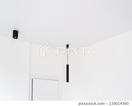 Minimalist interior showcasing modern black linear pendant and spot lights against a white brick wall and clean ceiling Minimalist interior showcasing modern black linear pendant and spot lights against a white brick wall and clean ceiling 139014360