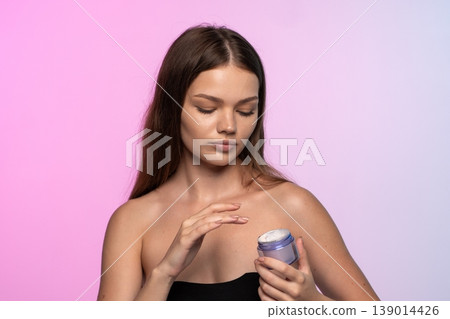 Woman closing eyes while applying a hydrating face cream to her skin, practicing a daily self-care beauty routine 139014426