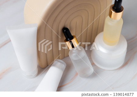 Skincare cosmetic products with serum dropper bottles and cream containers on minimal beige podium, beauty skincare routine concept 139014877