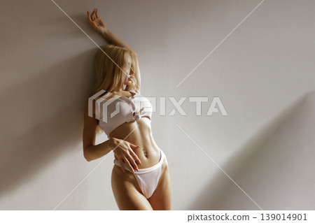 Sexy slim woman posing in white lingerie with toned body and flat stomach, fitness and body care concept in studio light Sexy slim woman posing in white lingerie with toned body and flat stomach, fitness and body care concept in studio light 139014901