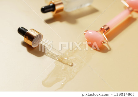 Cosmetic serum dropper and facial roller with skincare liquid texture on warm pastel background, beauty treatment concept Cosmetic serum dropper and facial roller with skincare liquid texture on warm pastel background, beauty treatment concept 139014905