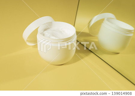 Open cosmetic cream jar with moisturizer reflected in mirror on yellow background in warm sunlight, skincare concept 139014908