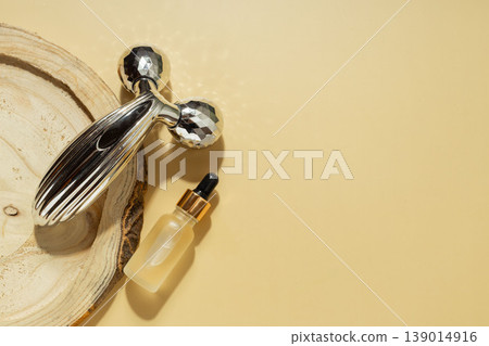 Facial massage roller and cosmetic serum dropper bottle on wooden slice with warm sunlight, skincare beauty concept 139014916