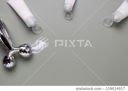 Metal facial roller with moisturizing skincare cream and cosmetic jar on neutral background, beauty treatment concept Metal facial roller with moisturizing skincare cream and cosmetic jar on neutral background, beauty treatment concept 139014917