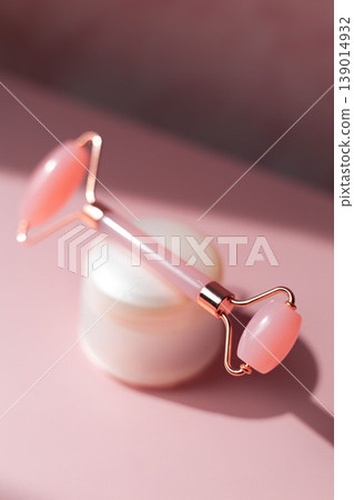 Rose quartz facial roller with cosmetic cream jar on pink background, skincare massage tool for beauty routine and face care 139014932
