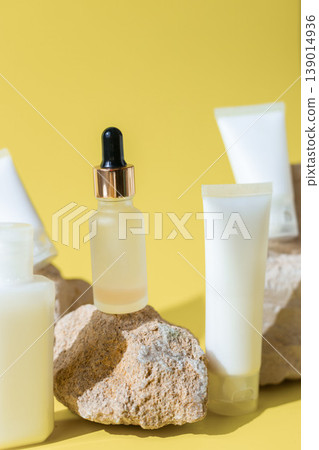 Cosmetic serum dropper bottle with skincare lotion tubes on natural stones and yellow background, beauty skincare product concept 139014936
