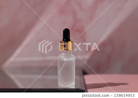 Cosmetic serum dropper with clear liquid and frosted glass bottle on pink reflective surface, skincare essence texture, beauty product concept Cosmetic serum dropper with clear liquid and frosted glass bottle on pink reflective surface, skincare essence texture, beauty product concept 139014953