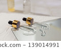 Glass cosmetic droppers with transparent serum on mirror surface, skincare essence drops and reflection, beauty treatment concept, minimalist cosmetic product background. 139014991