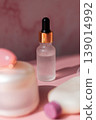 Cosmetic serum dropper with clear liquid and frosted glass bottle on pink reflective surface, skincare essence texture, beauty product concept 139014992