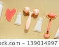 Flat lay skincare beauty routine with cosmetic bottles, serum dropper, facial roller, massage tool and towel on warm pastel background 139014997