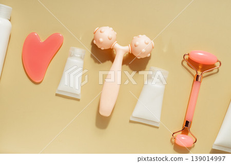 Flat lay skincare beauty routine with cosmetic bottles, serum dropper, facial roller, massage tool and towel on warm pastel background Flat lay skincare beauty routine with cosmetic bottles, serum dropper, facial roller, massage tool and towel on warm pastel background 139014997
