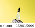 Cosmetic serum dropper bottle on natural stone with bright yellow background, skincare oil beauty product concept 139015000