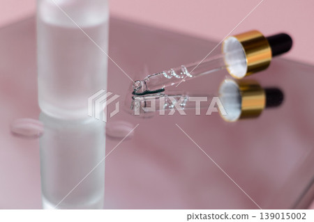 Cosmetic serum dropper with clear liquid and frosted glass bottle on pink reflective surface, skincare essence texture, beauty product concept Cosmetic serum dropper with clear liquid and frosted glass bottle on pink reflective surface, skincare essence texture, beauty product concept 139015002