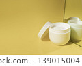 Open cosmetic cream jar with moisturizer reflected in mirror on yellow background in warm sunlight, skincare concept 139015004