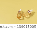Two cosmetic serum dropper bottles with golden liquid on pastel yellow background in warm sunlight, skincare concept 139015005