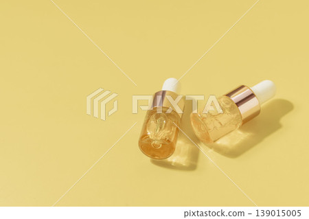 Two cosmetic serum dropper bottles with golden liquid on pastel yellow background in warm sunlight, skincare concept Two cosmetic serum dropper bottles with golden liquid on pastel yellow background in warm sunlight, skincare concept 139015005