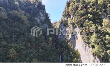 [Aerial view] The sheer cliffs of Sounkyo Gorge, beginning to be tinged with autumn colors, and the mountains towering in the distance (Hokkaido) 139015430