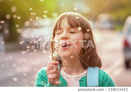 Child 8 years old releasing dandelion seeds in sunlight on city road background Child 8 years old releasing dandelion seeds in sunlight on city road background 139015452
