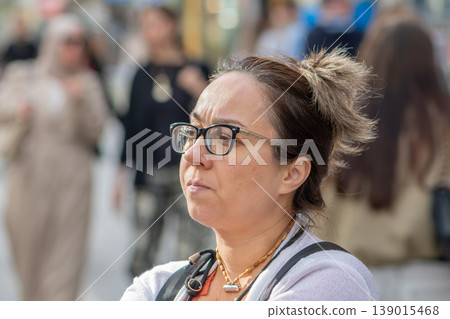Woman age 45 with glasses stands on a city street and looks aside. Woman age 45 with glasses stands on a city street and looks aside. 139015468