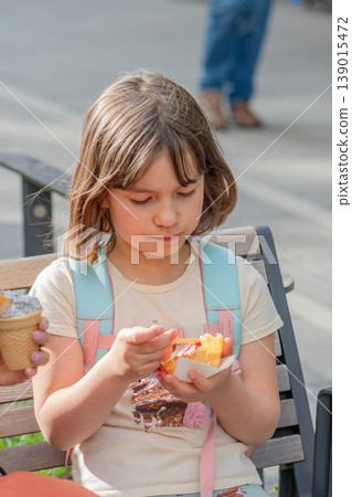 Girl age 7 eats ice cream on a bench during a walk through the city. Girl age 7 eats ice cream on a bench during a walk through the city. 139015472