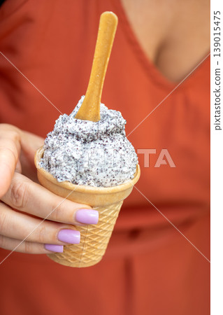 Unusual ice cream in waffle cone is shown in close up and held in woman hand. 139015475