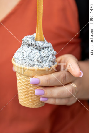 Light ice cream with dark crumbs is served in a waffle cone and held by woman hand. Light ice cream with dark crumbs is served in a waffle cone and held by woman hand. 139015476
