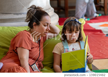 Woman and child reading colorful book together developing learning communication and family interaction Woman and child reading colorful book together developing learning communication and family interaction 139015482