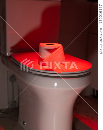 Toilet paper on toilet lid with red light. Symbolic representation of bowel movement issue and digestive health problem. photography 139016137
